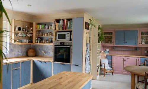 Cozy kitchen with colorful cabinets, open shelves, and a microwave. There's a dining area with wooden chairs.