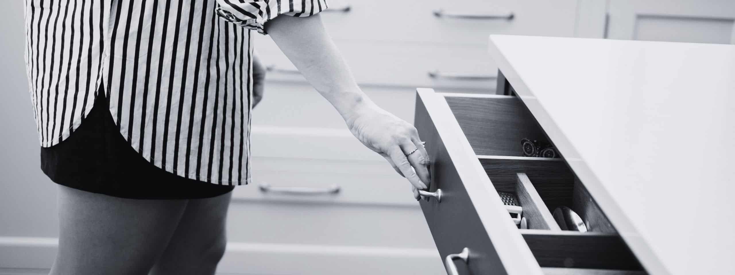 Person opening a kitchen drawer in a modern setting, wearing a striped shirt.