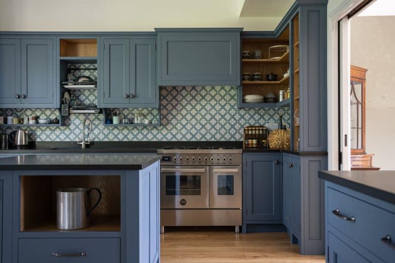 A modern kitchen with blue cabinets, patterned tiles, and stainless steel appliances.