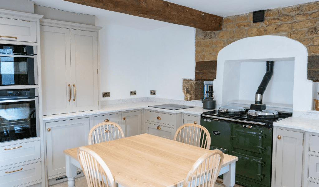 Rustic kitchen with wooden table, chairs, stone accent, and a traditional green stove.