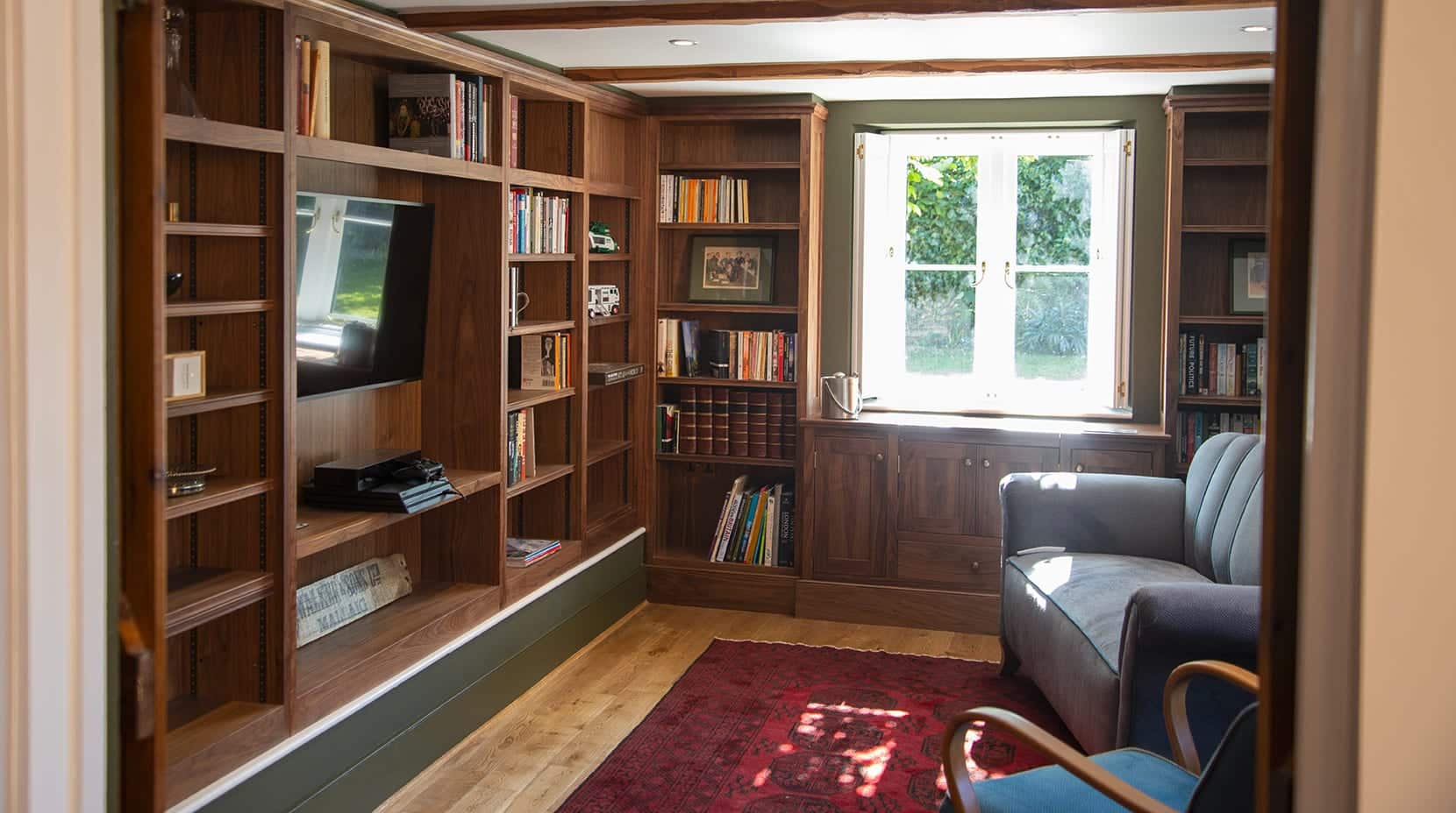 Cozy room with wooden bookshelves, a TV, armchair, and window letting in natural light.