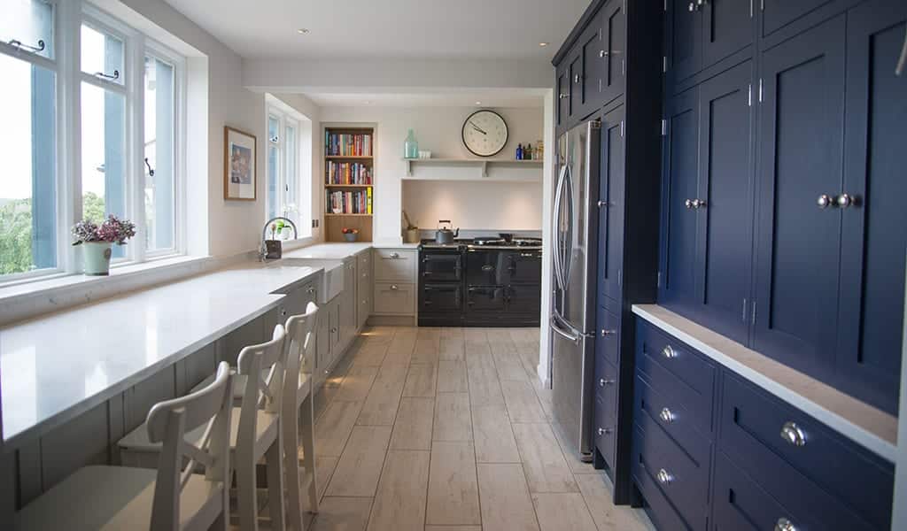 Modern kitchen with blue cabinets, white countertops, wooden floor, and a large window.