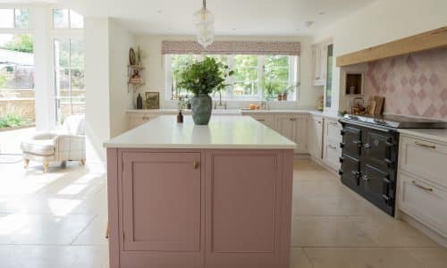 Bright kitchen with a pink island, white countertops, and large windows letting in natural light.