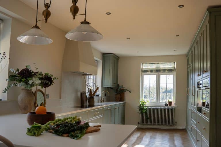 Spacious kitchen with white and navy cabinets, wooden floor, and bar seating under large windows.